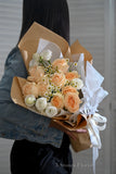 Bouquet of peach and white roses wrapped in brown paper 