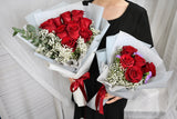 Person holding two bouquets of red roses with white baby's breath.